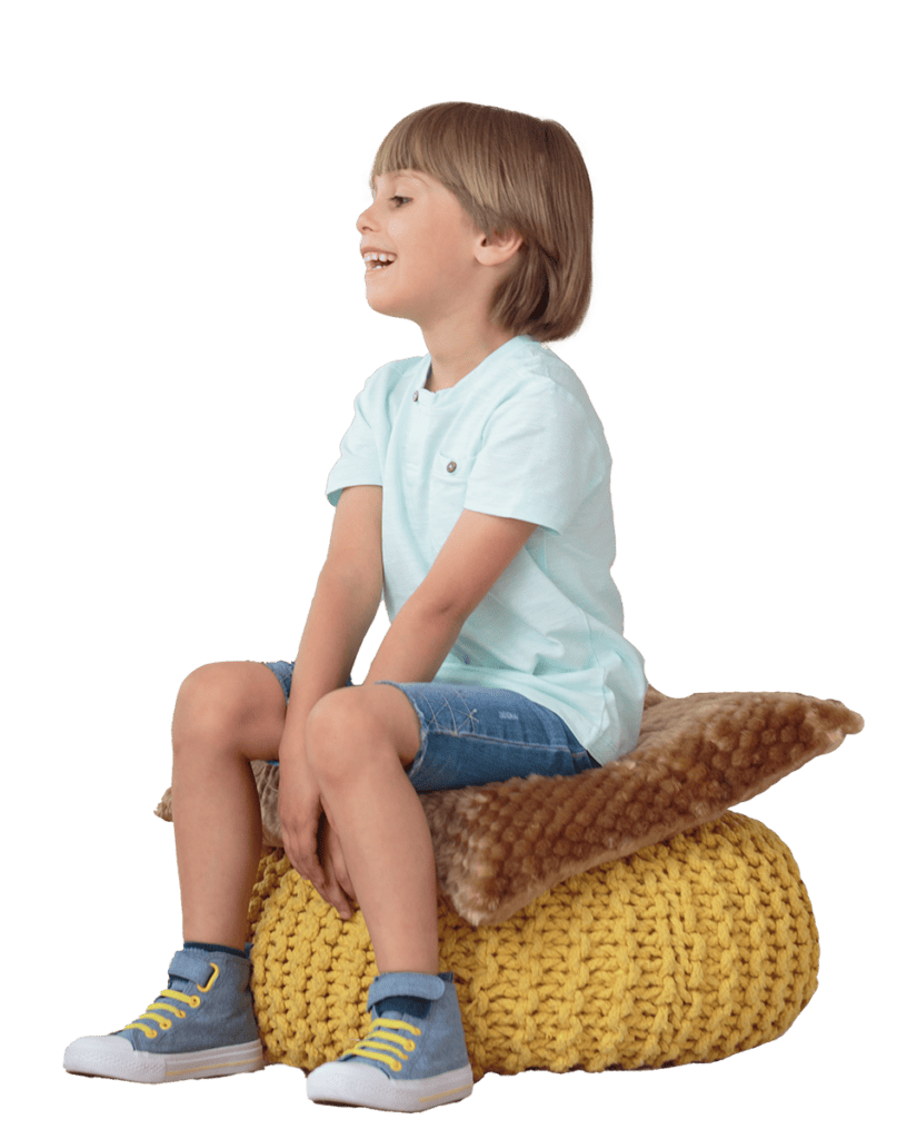 A young boy talks to someone off frame while sitting on a yellow cushion.