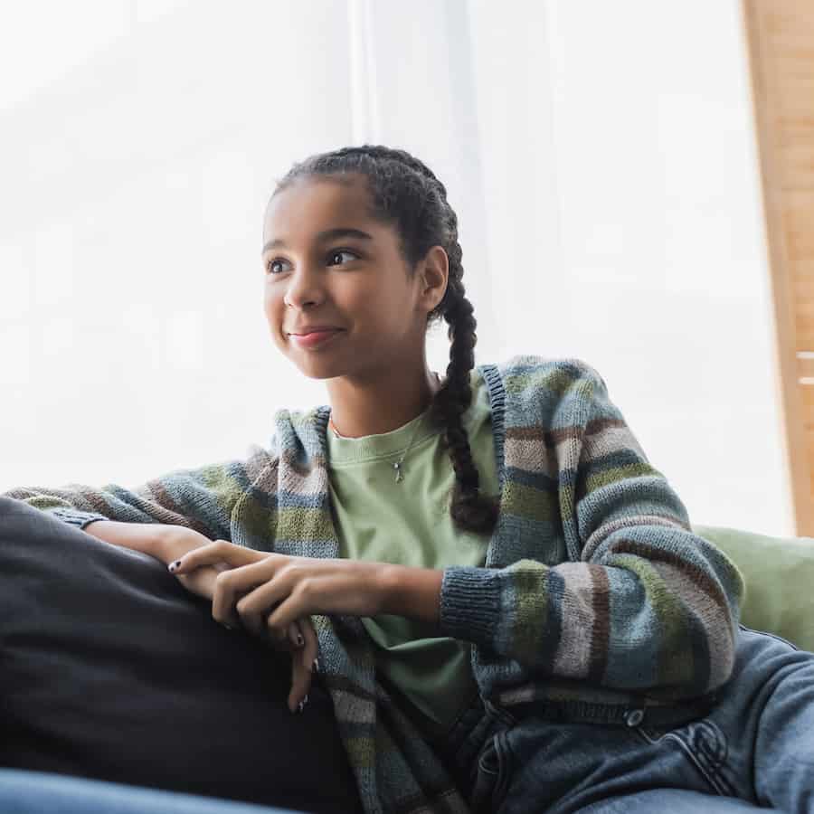 A teen girl sits comfortably on a green chair.