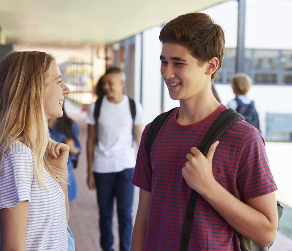 Two teens in high school talk in a hallway.